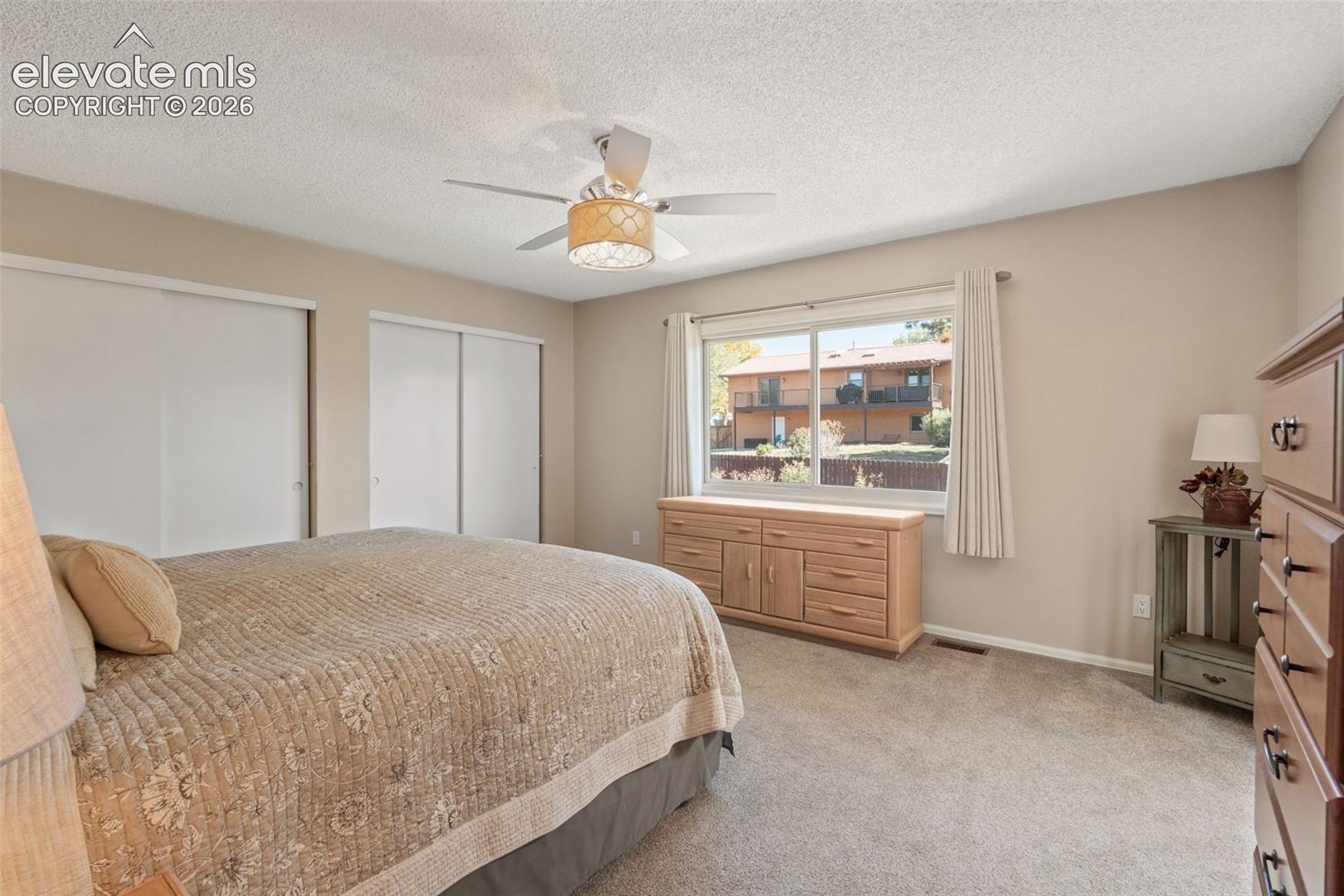 Room featuring neutral wall tones, wall-to-wall carpeting, dual sliding-door closets, and a ceiling fan with integrated drum lighting
