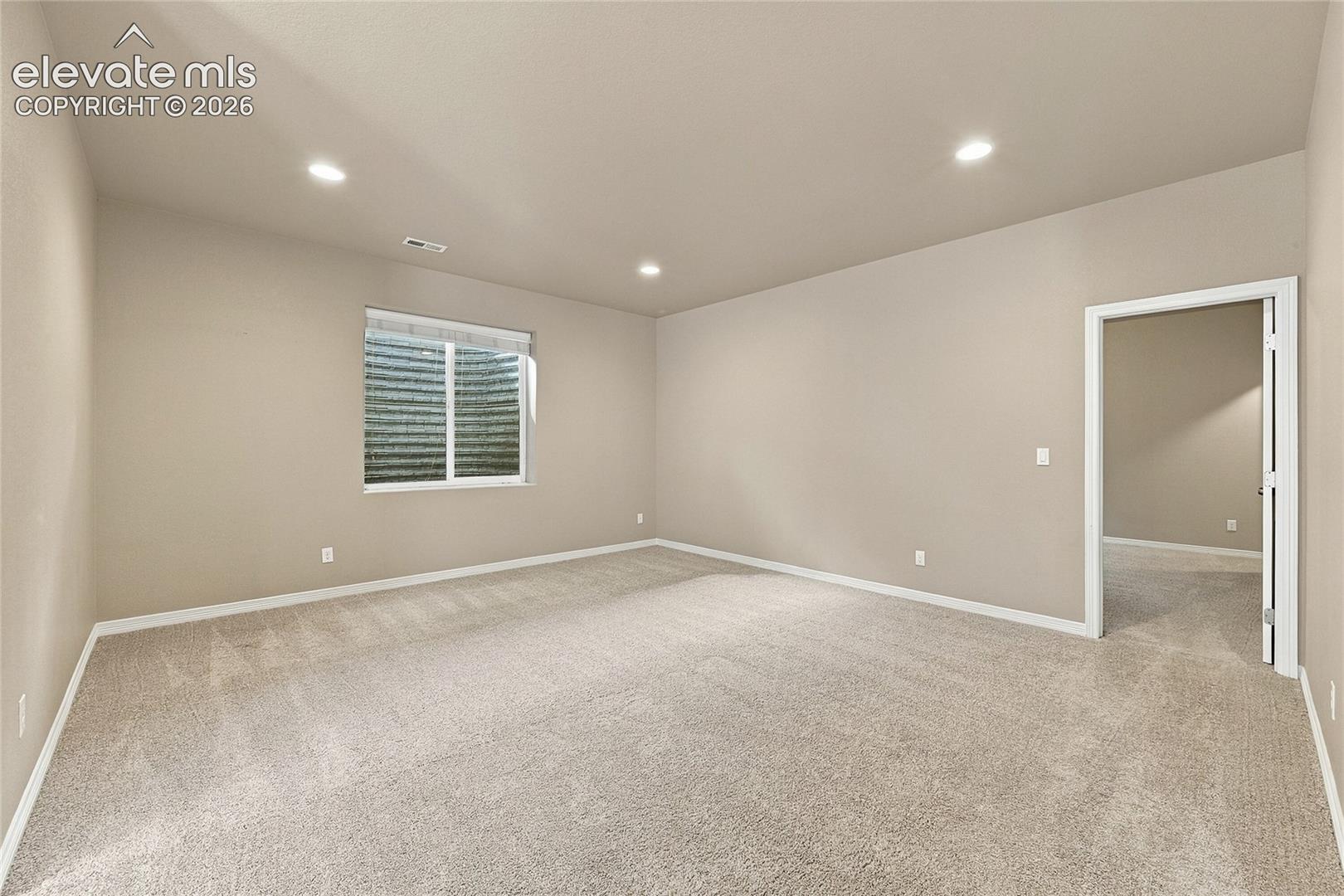 Neutral interior space featuring high ceilings, wall-to-wall carpeting, recessed lighting, and a window with an egress well