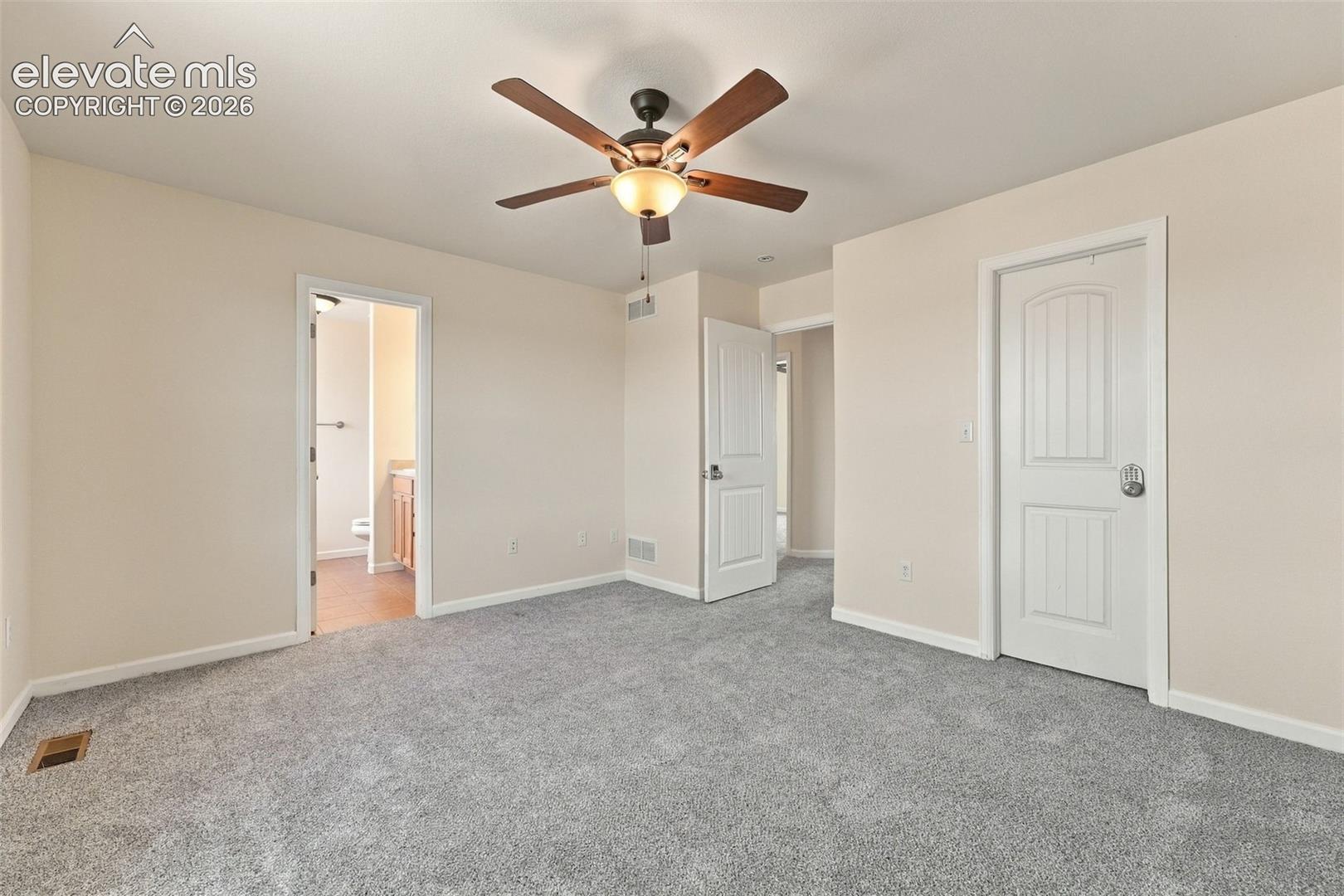 Neutral-toned interior space featuring gray wall-to-wall carpeting, a central ceiling fan with integrated lighting, and white paneled doors