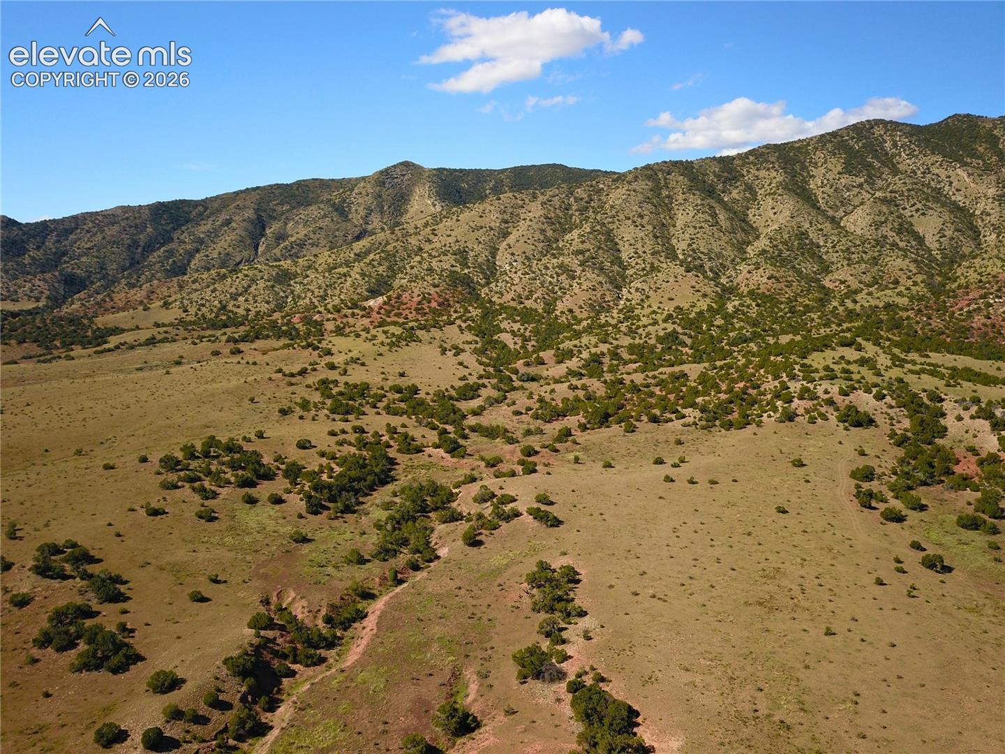 Expansive natural terrain featuring varied topography, scattered green vegetation, and distant mountainous scenery under a clear sky