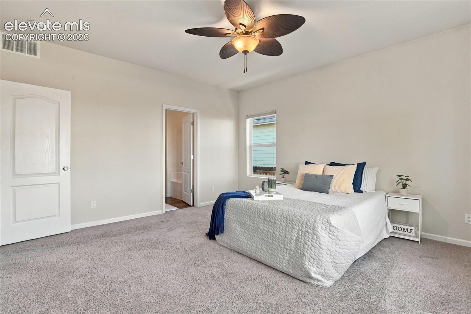 Neutral-toned carpeted flooring, multi-blade ceiling fan with integrated light fixture, single-panel interior doors, and window with casing trim