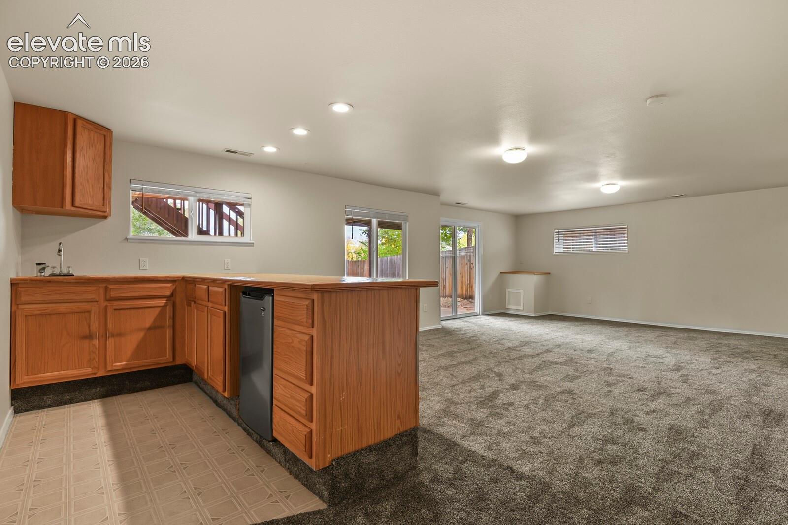 Kitchenette area featuring wood cabinetry,tile countertops, a wet bar sink, instant hot water tap, refrigerator, and recessed lighting