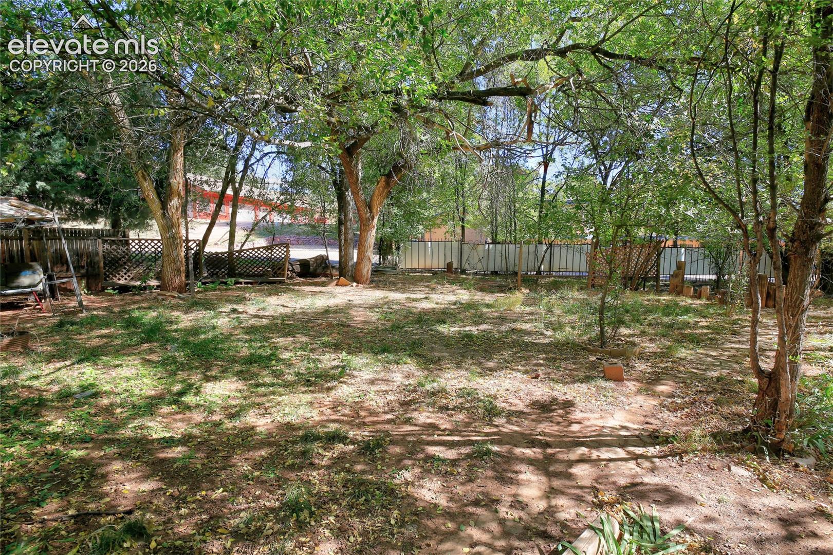 Backyard featuring mature trees, partial wood lattice fencing, and a metal perimeter fence