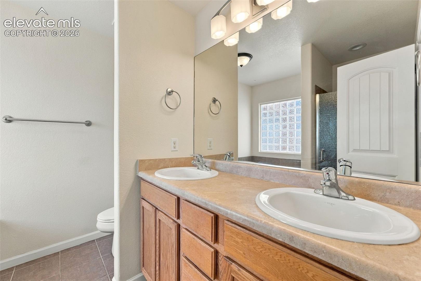 Bathroom vanity featuring dual under-mount sinks, integrated solid-surface countertop, wood-finish cabinetry, and a full-width mirror with overhead five-light fixture