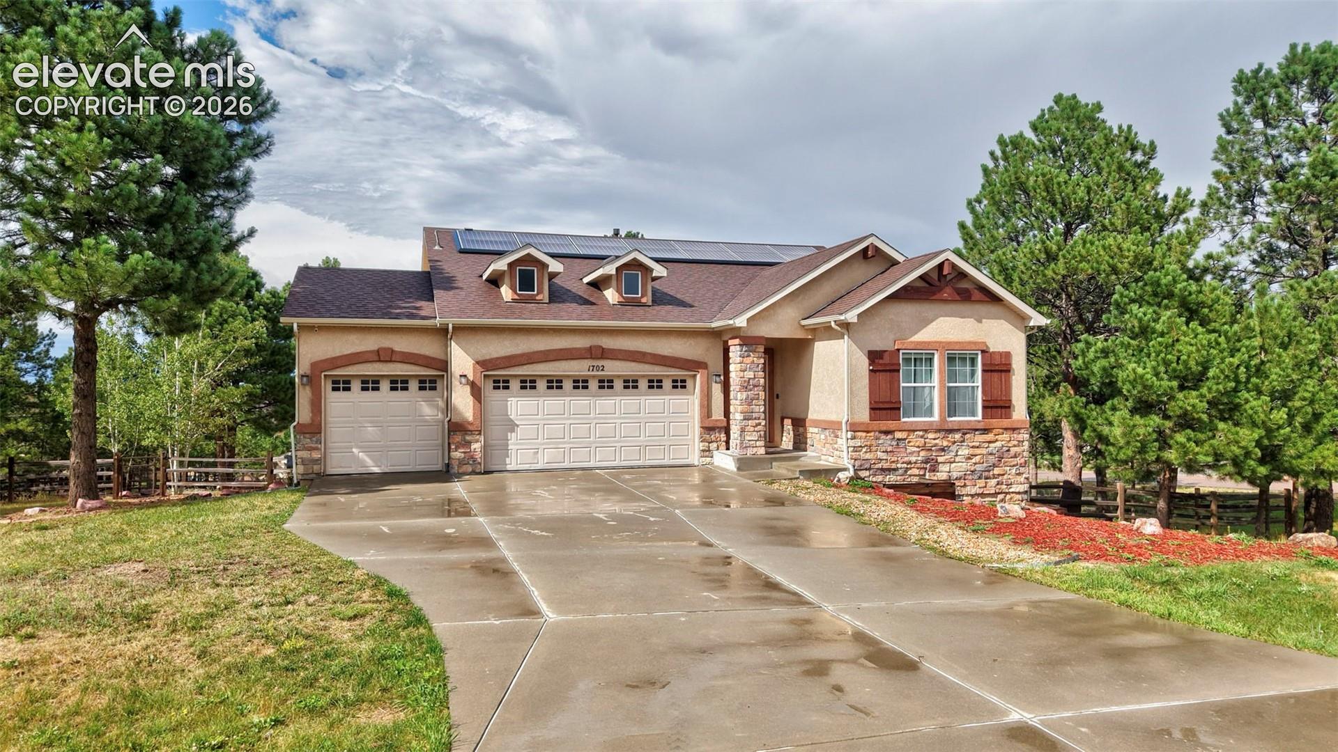 Stucco exterior featuring stone accents, a multi-car driveway, and mature trees