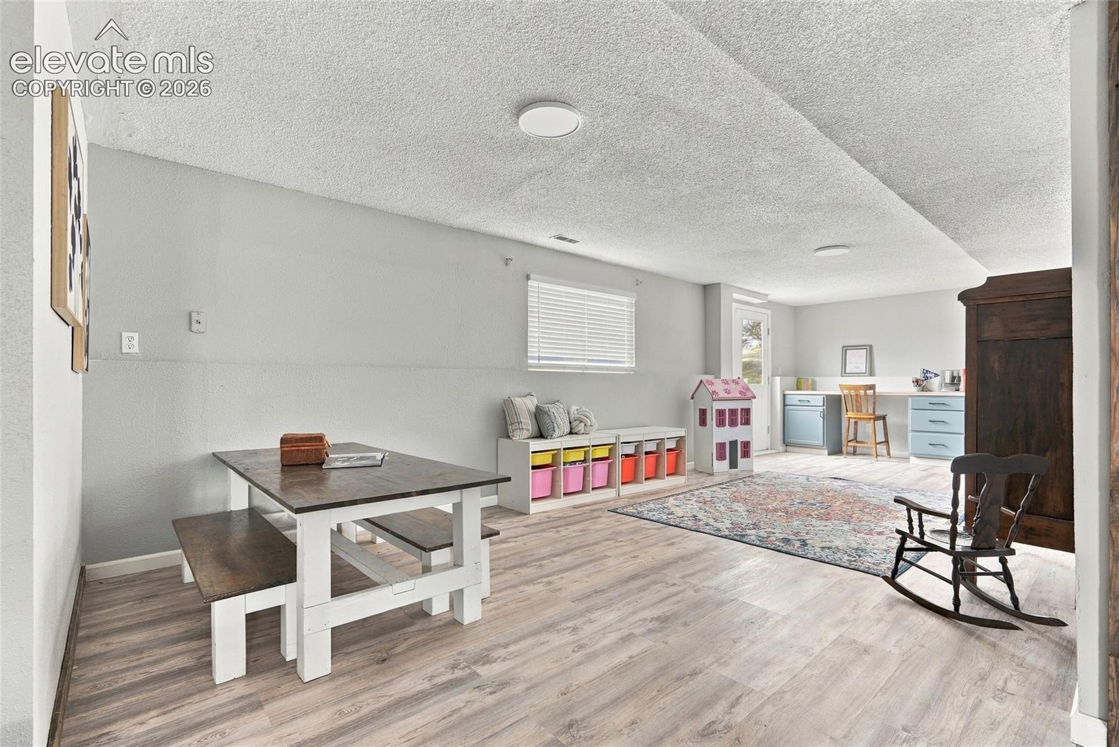 Light-toned wood-finish flooring, recessed lighting, white window blinds, light gray wall paint, and a built-in desk area with lower cabinetry