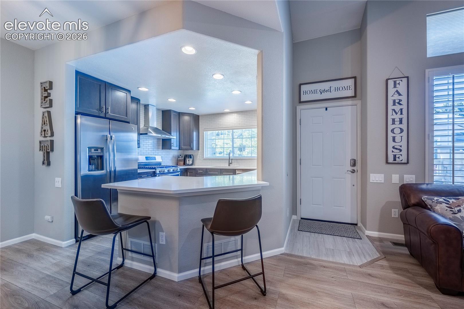 Kitchen featuring dark-toned cabinetry, stainless steel appliances, a peninsula with stone-surface countertop, and recessed ceiling lighting