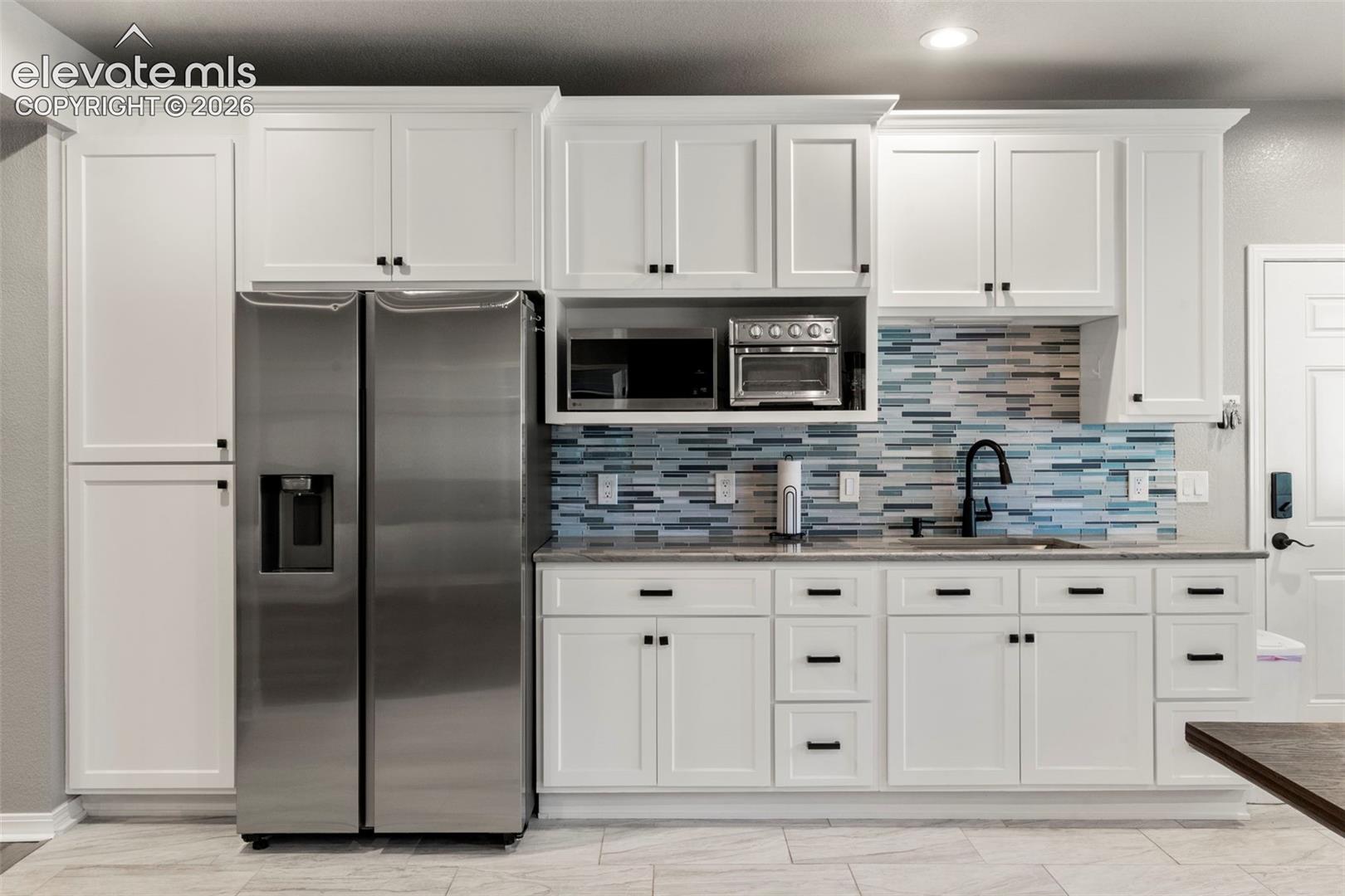 Kitchen with white cabinets, stainless steel appliances, light stone counters, and tasteful backsplash