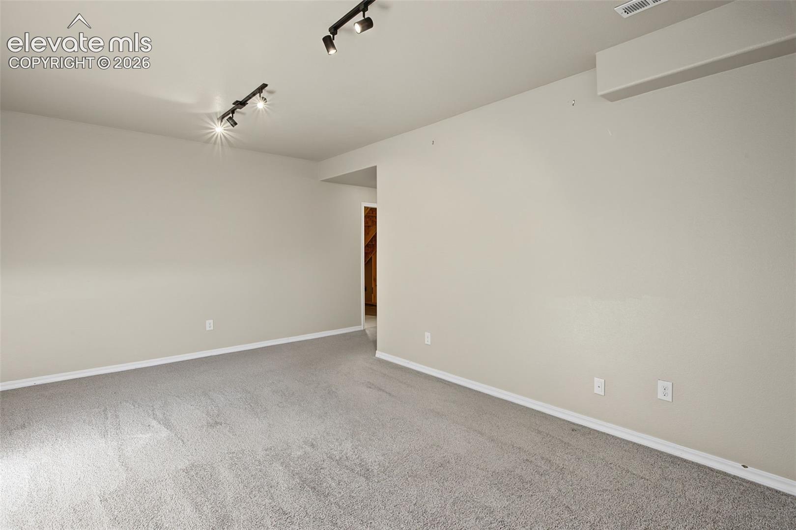 Neutral-toned interior space featuring light-colored wall-to-wall carpeting and adjustable dual-track ceiling lighting