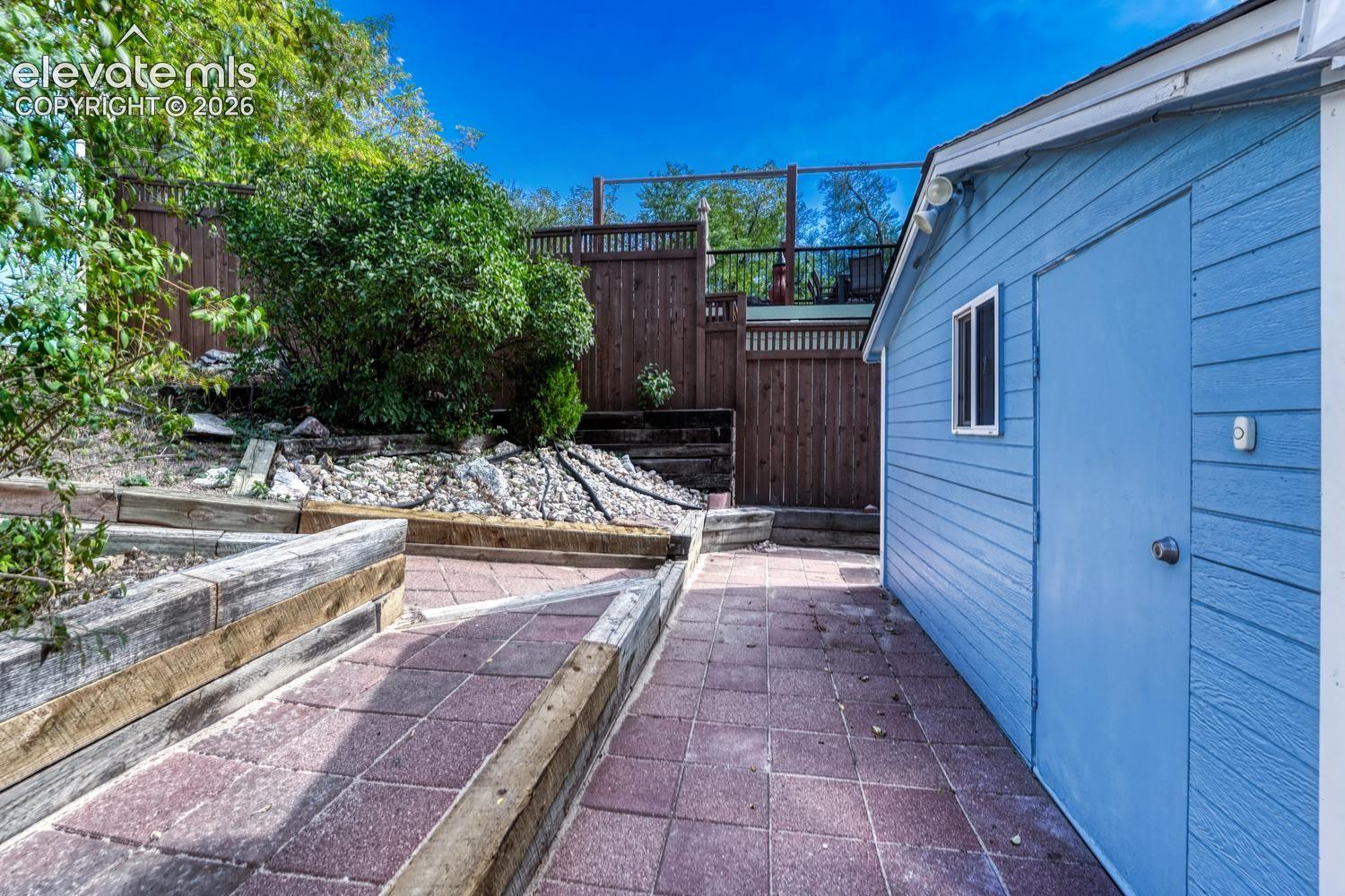 Red paver walkway leading to a light blue exterior structure with siding, a window, and a door
