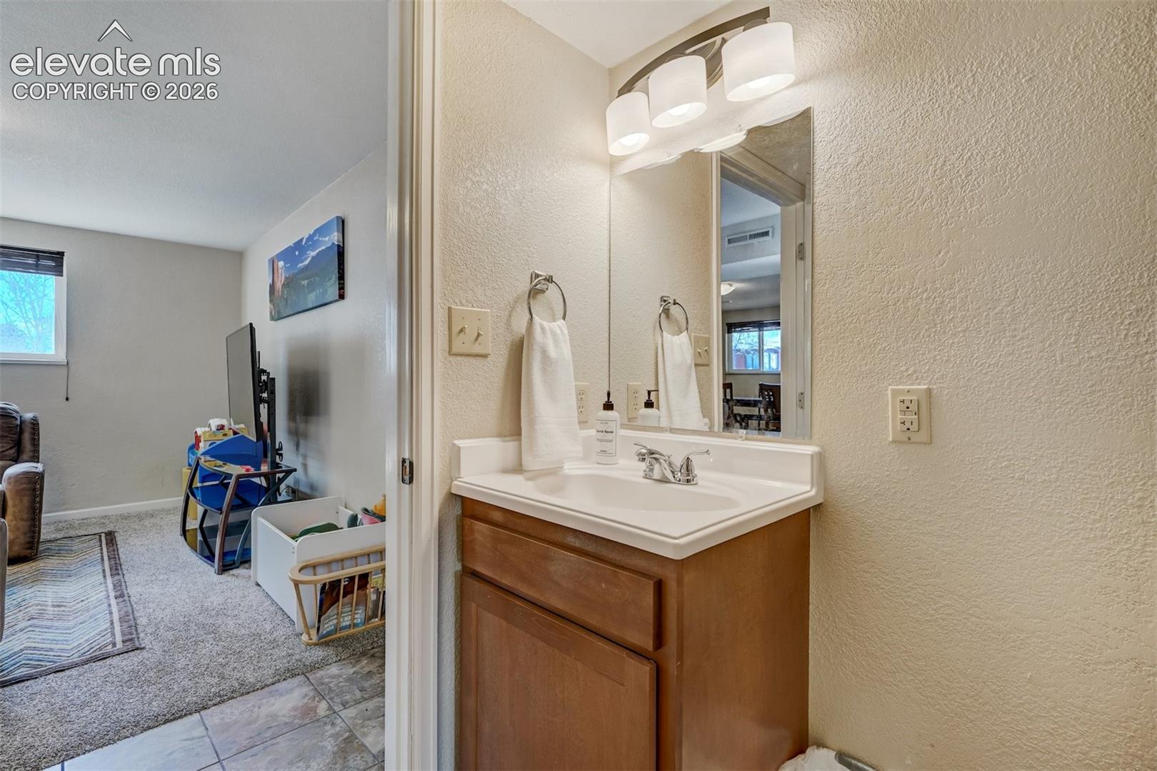 Vanity with wood-finish cabinetry, integrated sink, and wall-mounted light fixture
