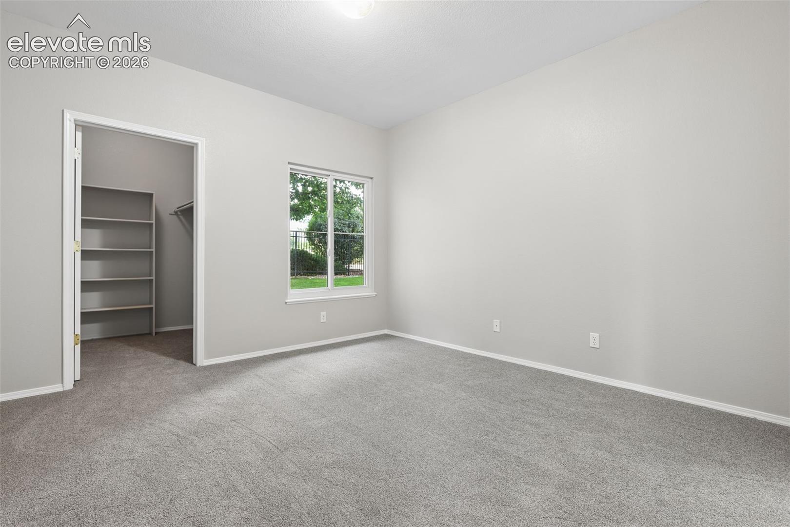 Carpeted room featuring a single window, an overhead light fixture, and a closet with shelving