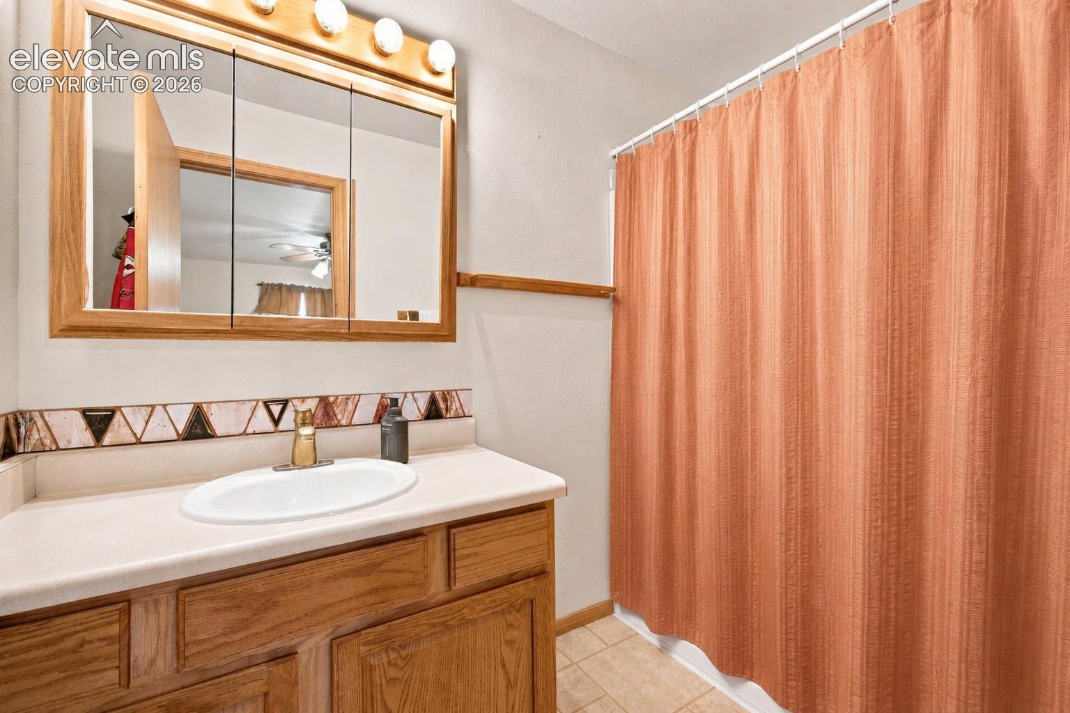 Wood-finish vanity with a light-toned countertop, oval undermount sink, and a framed medicine cabinet featuring integrated lighting