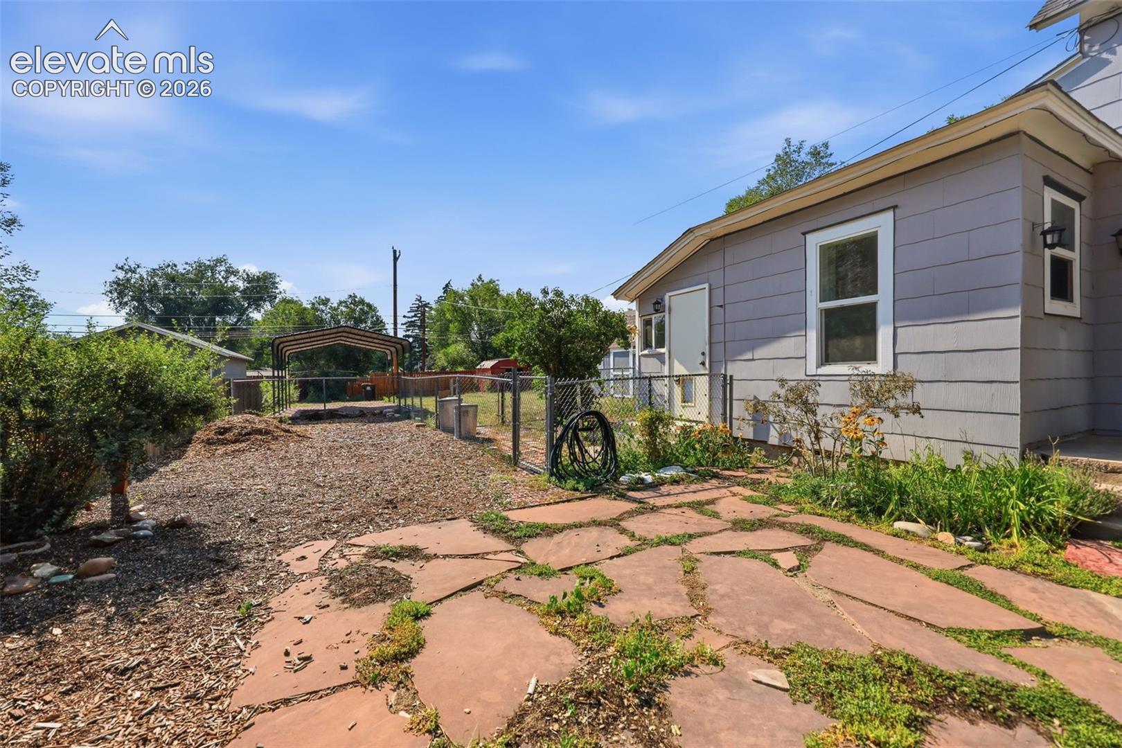 Exterior featuring a metal carport, horizontal siding, white trim windows, a side door yard access, and flagstone paving.