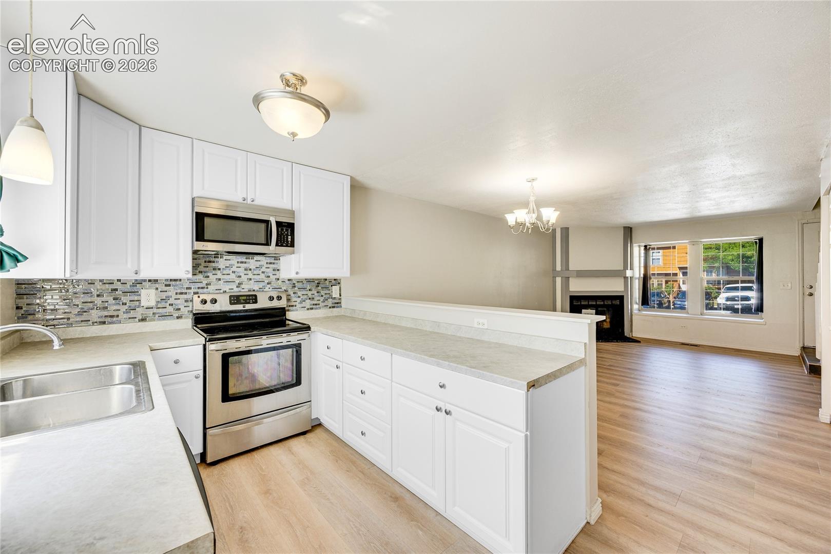 Kitchen featuring white cabinetry, stainless steel appliances, mosaic tile backsplash, and light-toned countertops