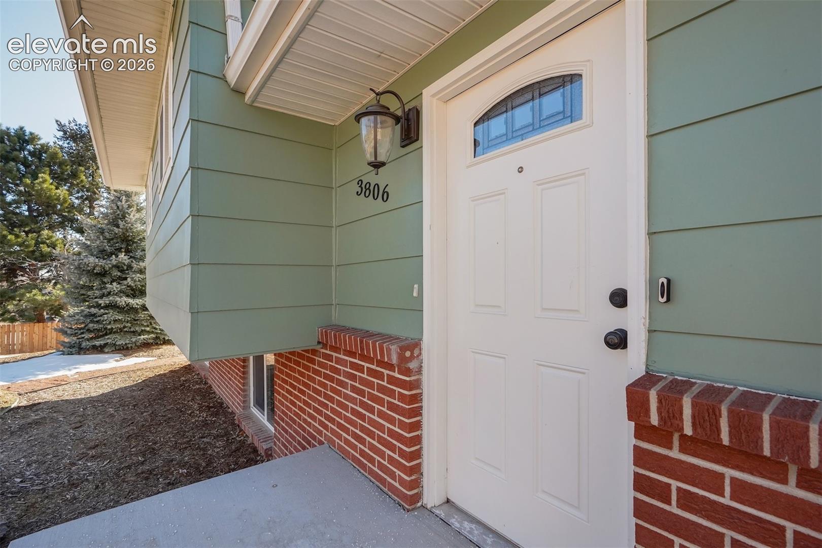Exterior featuring light green siding, a white front door with an arched window, and red brick detailing