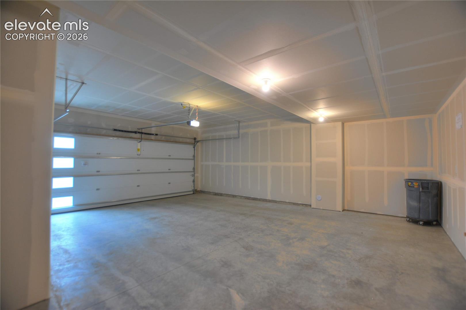 Spacious garage with an overhead door featuring frosted window panels, concrete flooring, and ceiling-mounted lighting fixtures