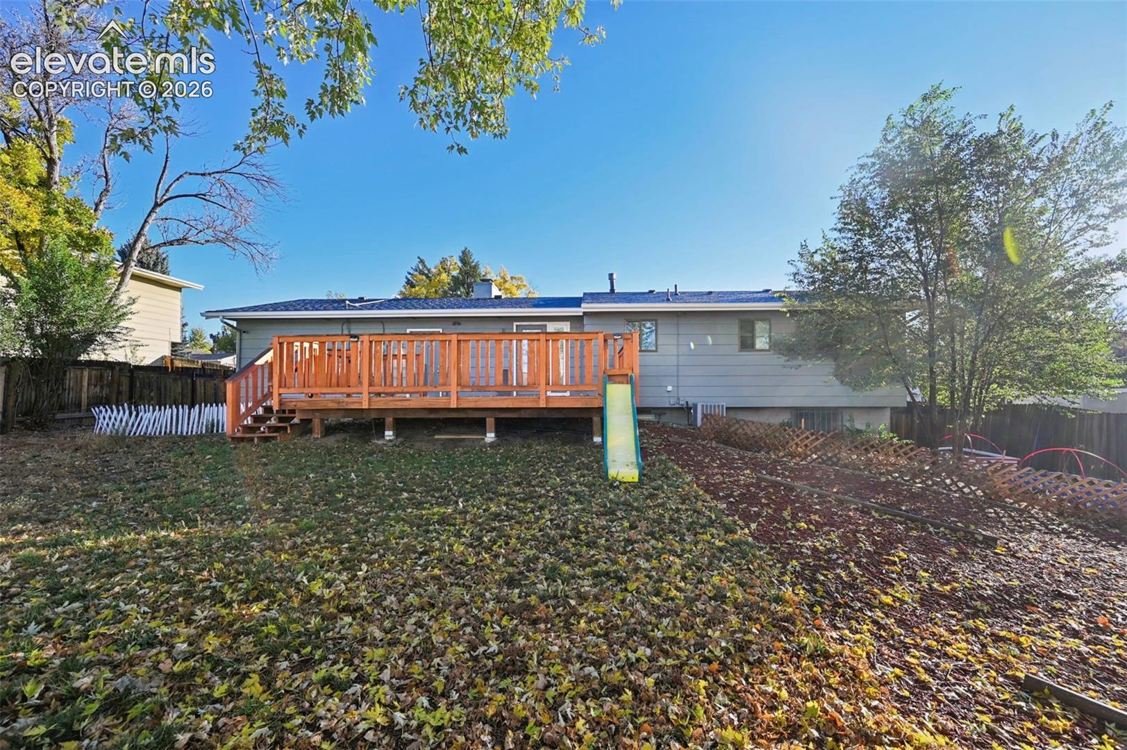 Backyard featuring a raised wooden deck with horizontal railing, wood-finish siding, and mature trees, garden beds, storage shed and more! 