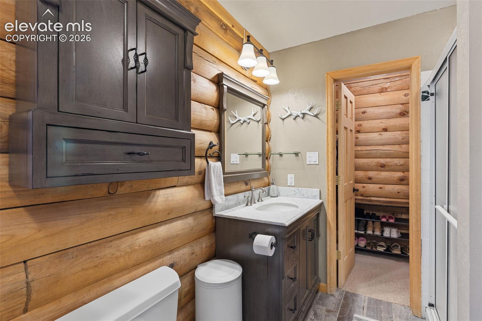 Bathroom featuring log walls, vanity with stone-style countertop and integrated sink, wall-mounted cabinetry, tri-light fixture, and glass-enclosed shower