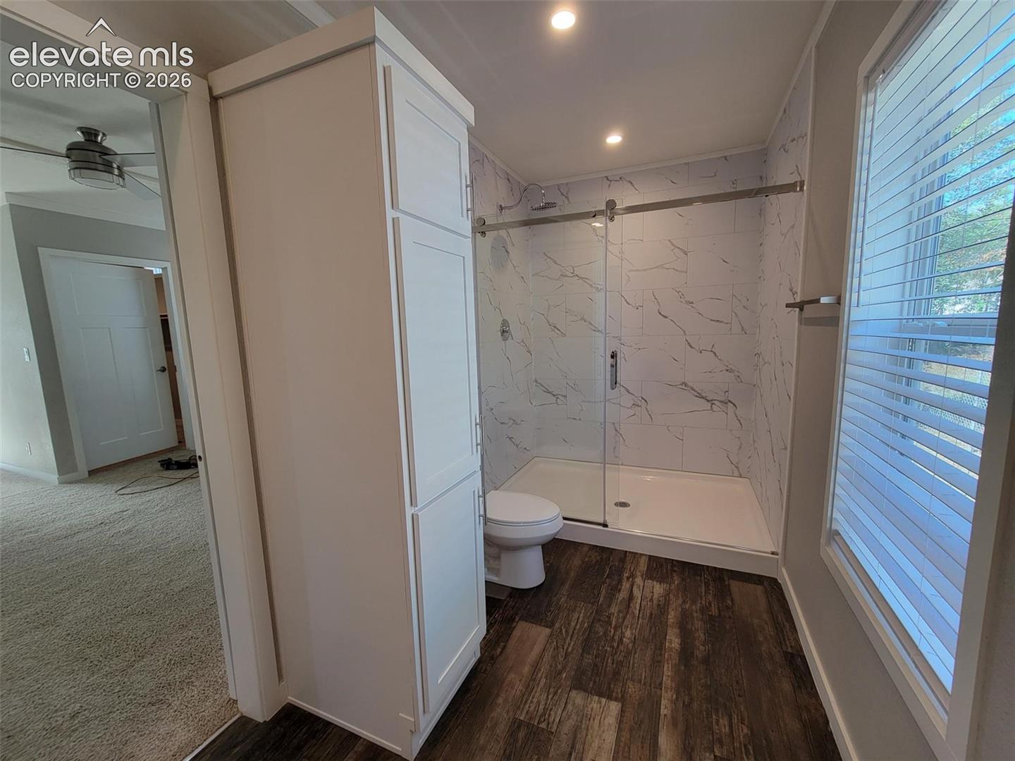 Bathroom featuring a walk-in shower with glass sliding doors, stone-patterned wall tile, built-in floor-to-ceiling cabinetry, and wood-finish flooring