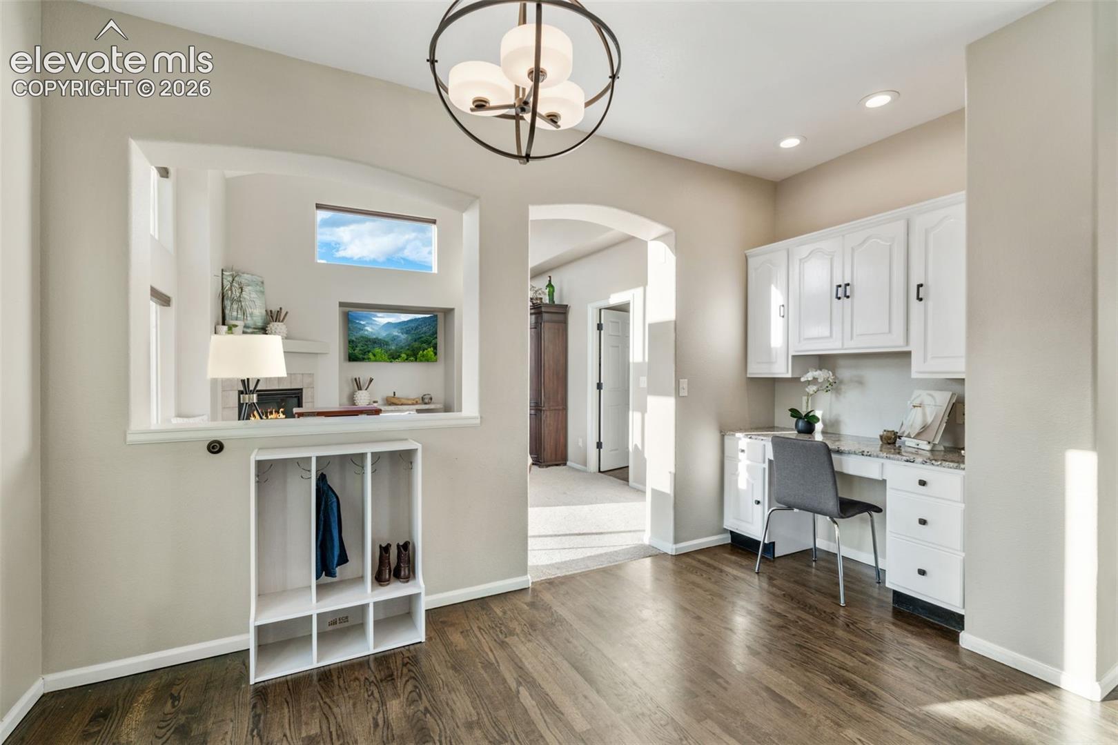 Built-in white cabinetry, stone-surface desk, wood-finish flooring, recessed lighting, and orb-style chandelier