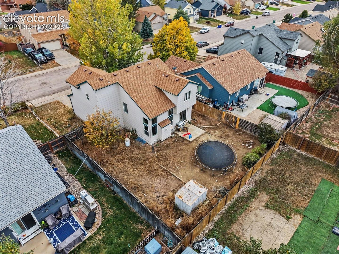 Two-story residence featuring light-toned horizontal siding, a multi-gabled asphalt shingle roof, tall vertical windows, a rear concrete patio, and a fenced-in perimeter
