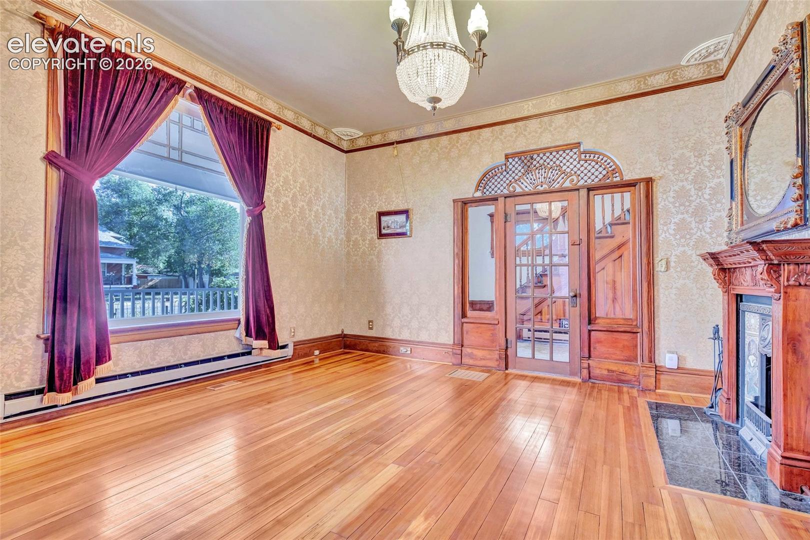 Wood-finish flooring, fireplace with a carved wooden mantel and stone hearth, intricate wood-framed glass door with arched transom, and a crystal chandelier