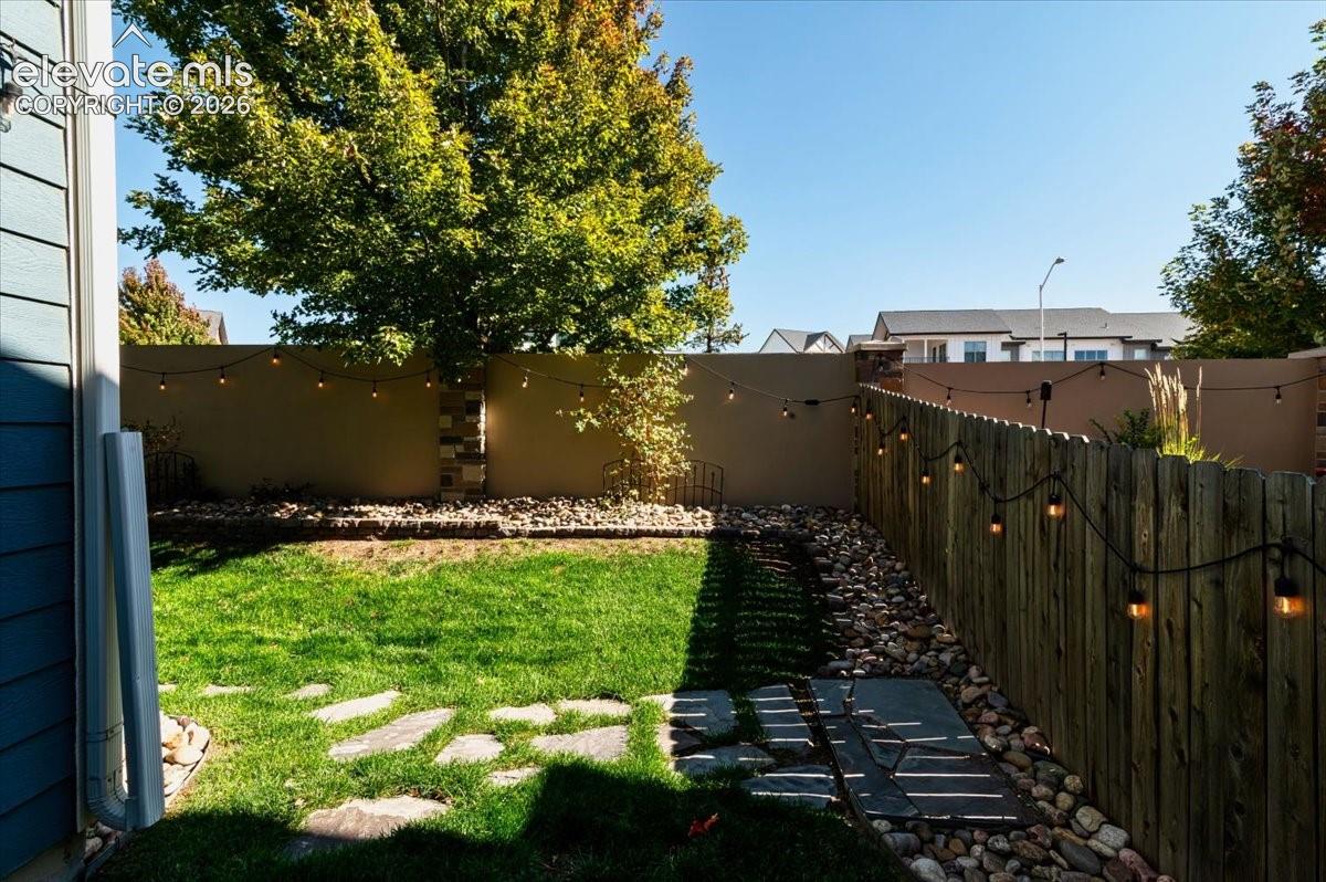 Manicured lawn with flagstone stepping stones, natural wood fencing, and a stucco privacy wall