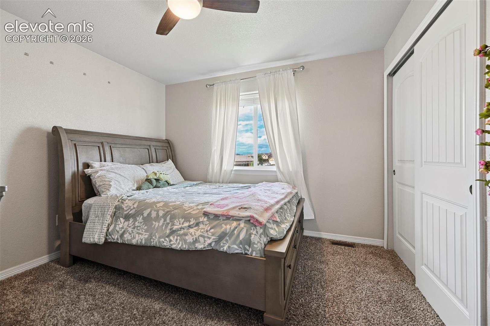 Carpeted flooring, window with natural light, ceiling fan with integrated lighting, and sliding closet doors