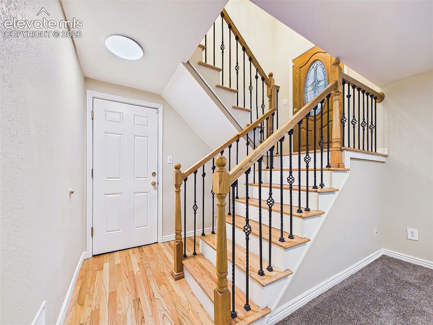 Welcoming entryway featuring hardwood flooring and a staircase with wood treads and decorative wrought-iron balusters that create an elegant first impression.