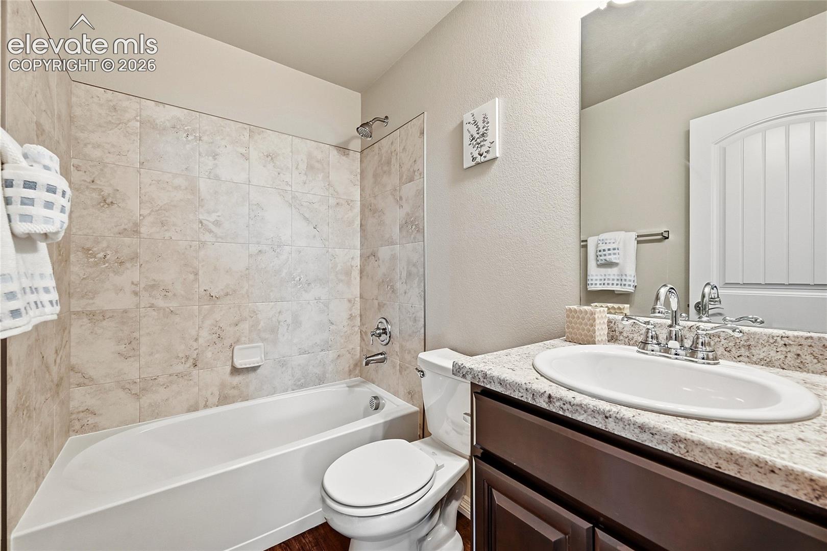 Bathroom featuring a built-in tub with neutral-toned tile surround, single vanity with an integrated sink, polished chrome faucet, and a large wall-mounted mirror