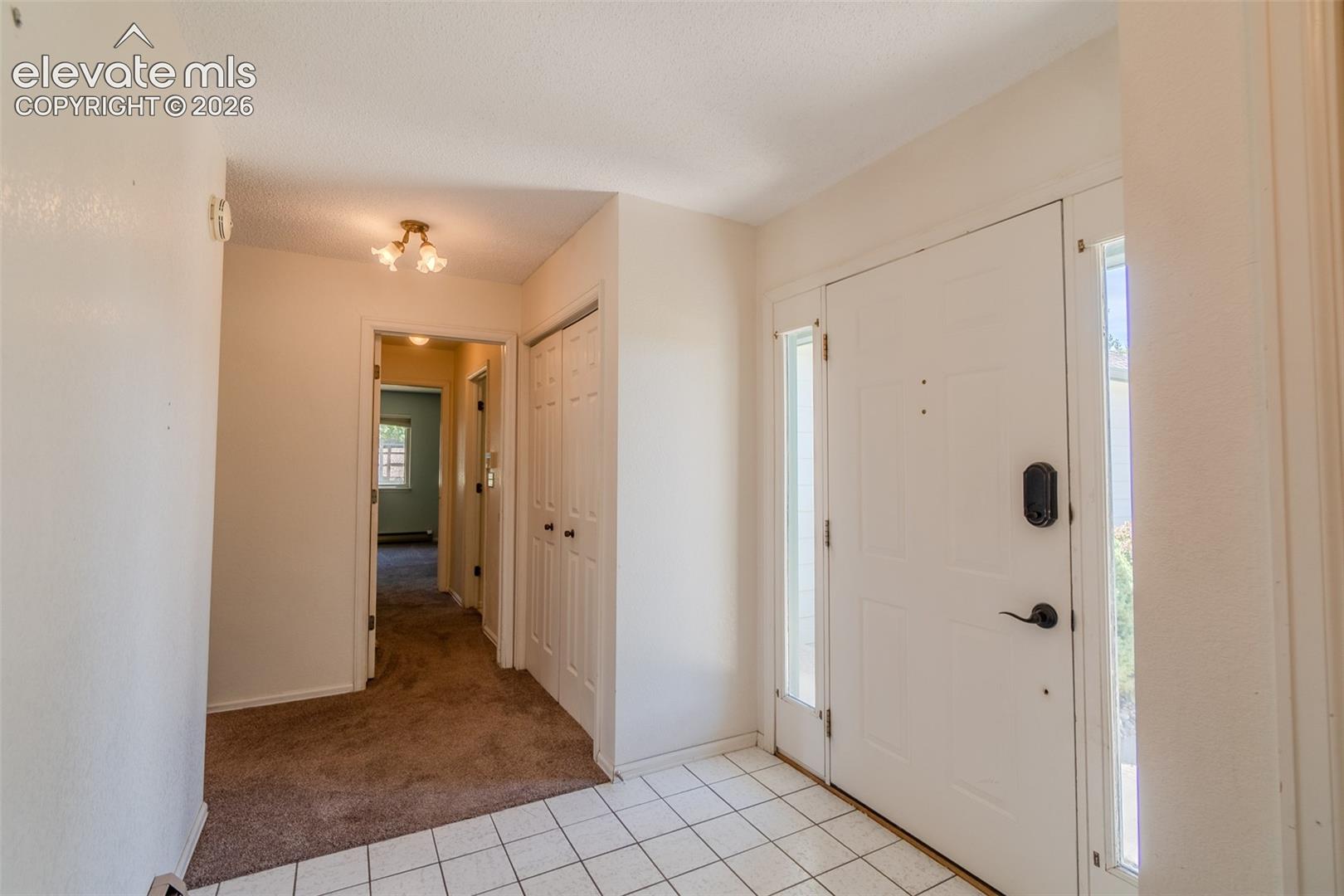 White paneled entry door with sidelight windows, tile flooring, and a hallway featuring carpet flooring and bi-fold closet doors