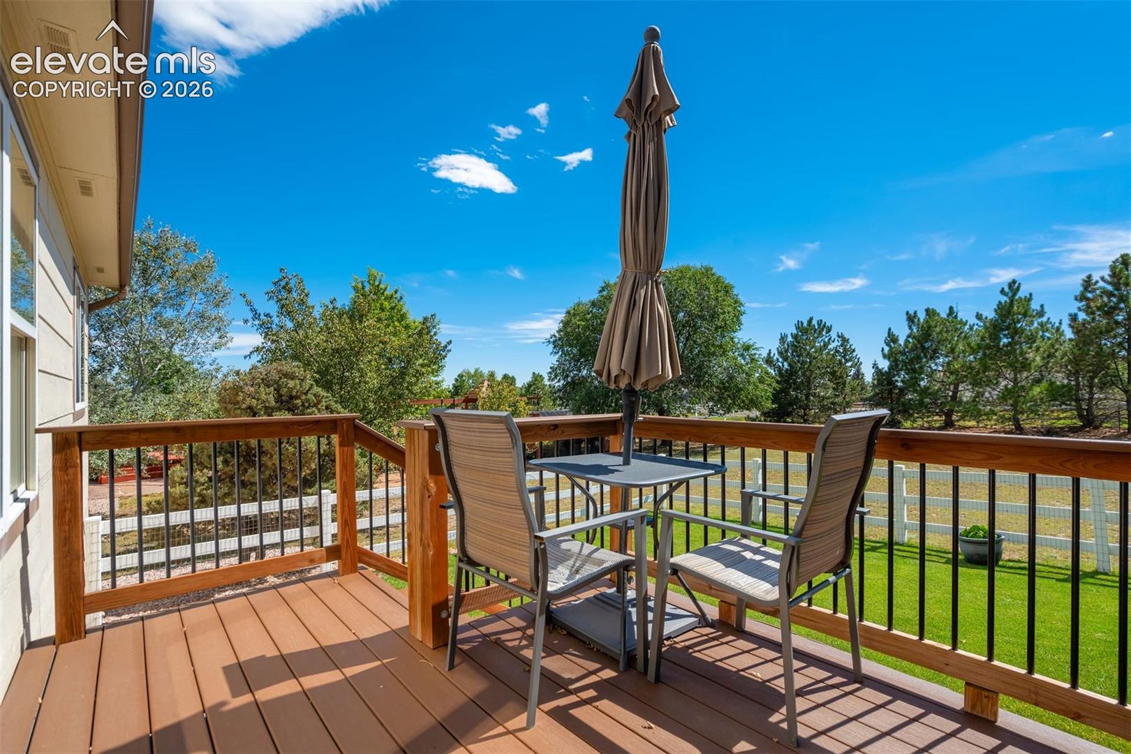 Elevated composite deck featuring composite decking, wood-finish railing posts, and black metal balusters, overlooking a grass yard enclosed by a white rail fence