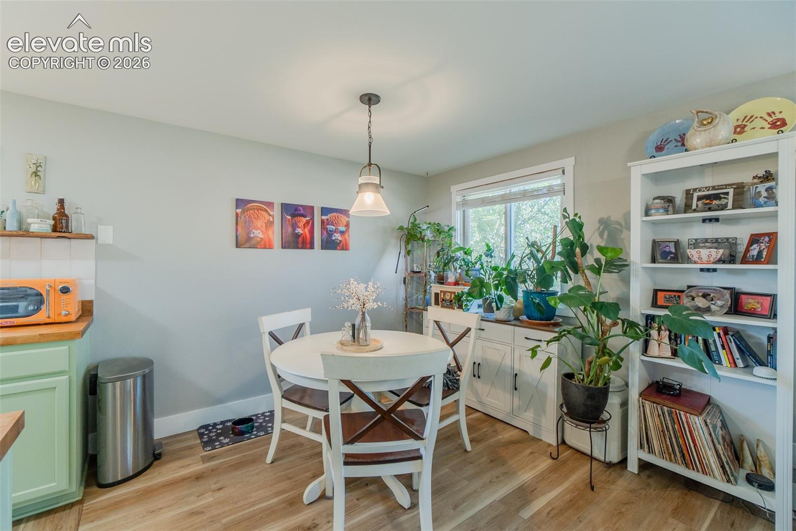 Dining area featuring wood-finish flooring, a contemporary pendant light fixture, a window with natural light, and a storage cabinet that will stay