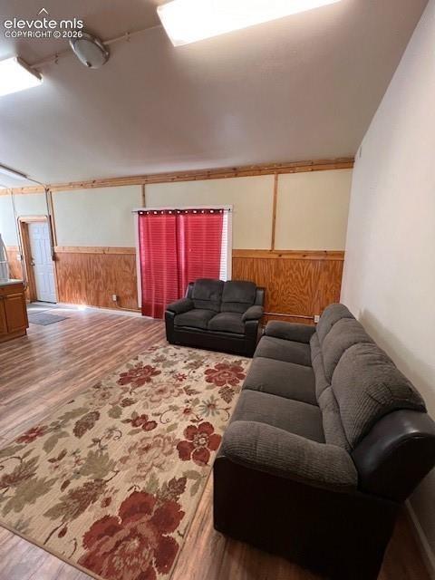 Wood-finish flooring, half-wall wood paneling with decorative trim, vaulted ceiling, and recessed entry door