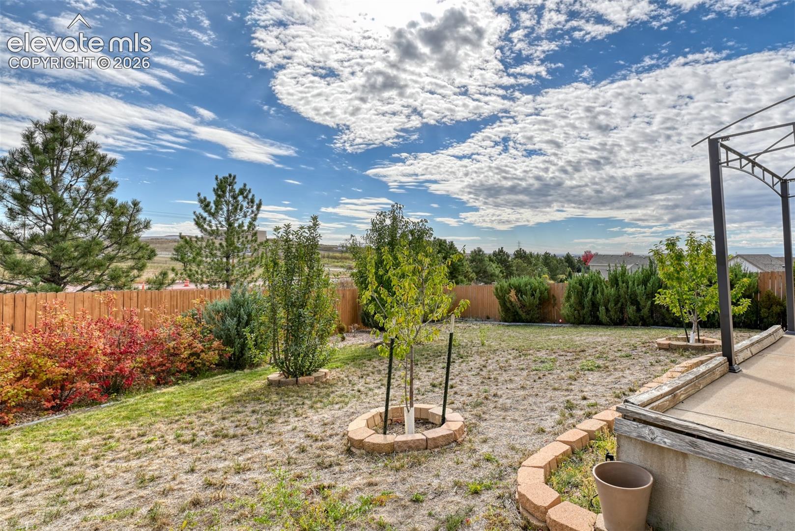 Rear yard featuring a concrete patio, stone-block landscaping borders, a wood fence, and established trees