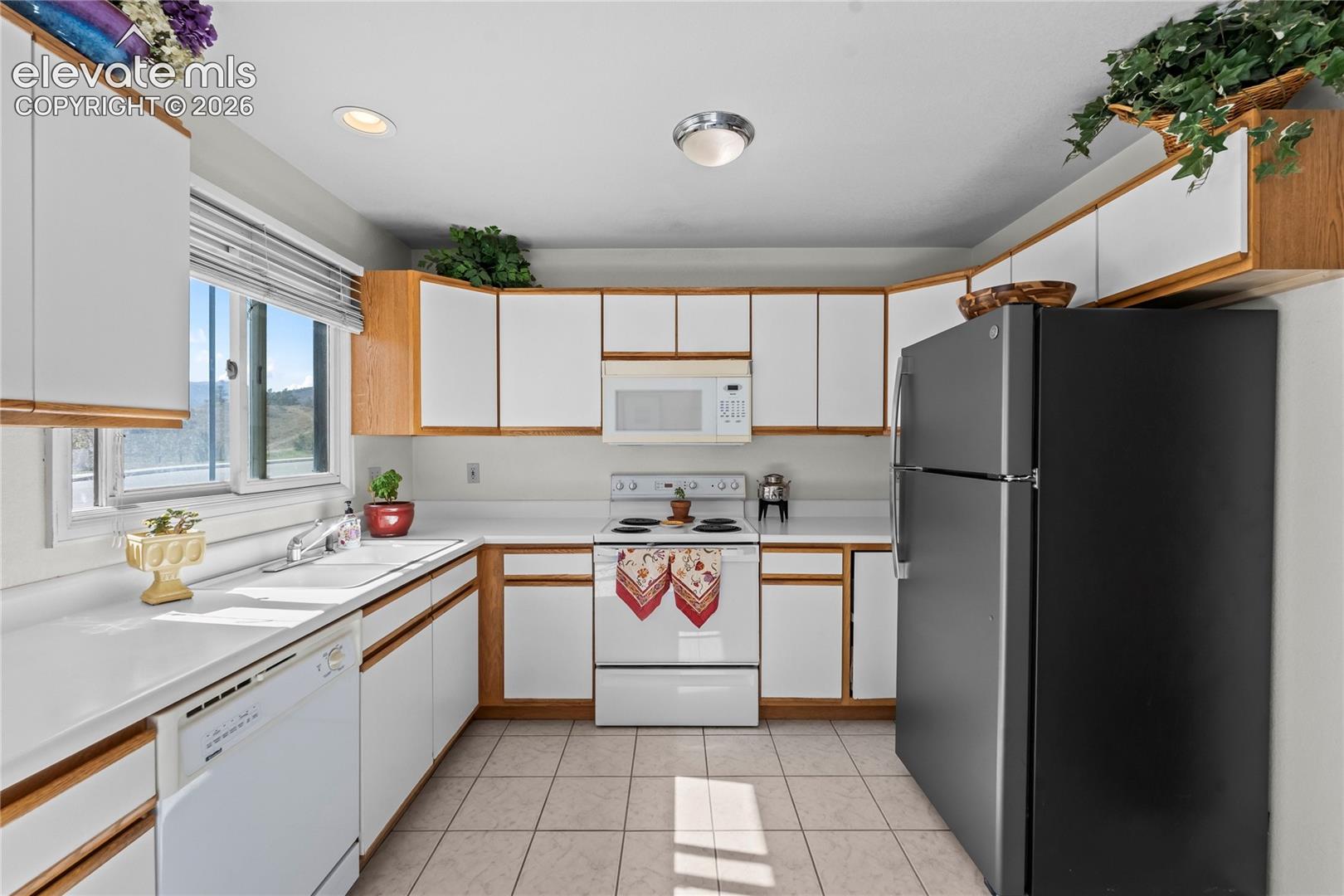 Efficient kitchen featuring white cabinetry with wood-finish trim, white countertops, tile flooring, and integrated white appliances