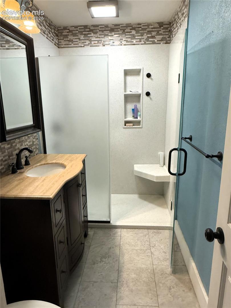 Bathroom featuring a dark wood vanity with a stone-top integrated sink, a glass-enclosed walk-in shower with a built-in corner seat, a recessed shower niche, and mosaic tile accents