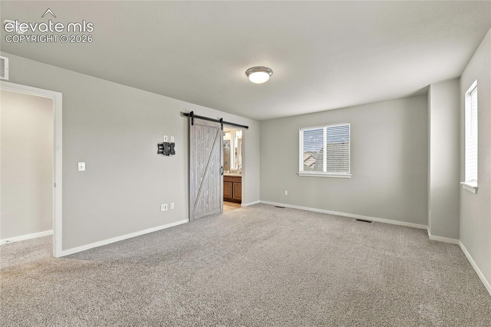 Carpeted interior with light gray walls, multiple windows, and a barn door entry to an adjoining area