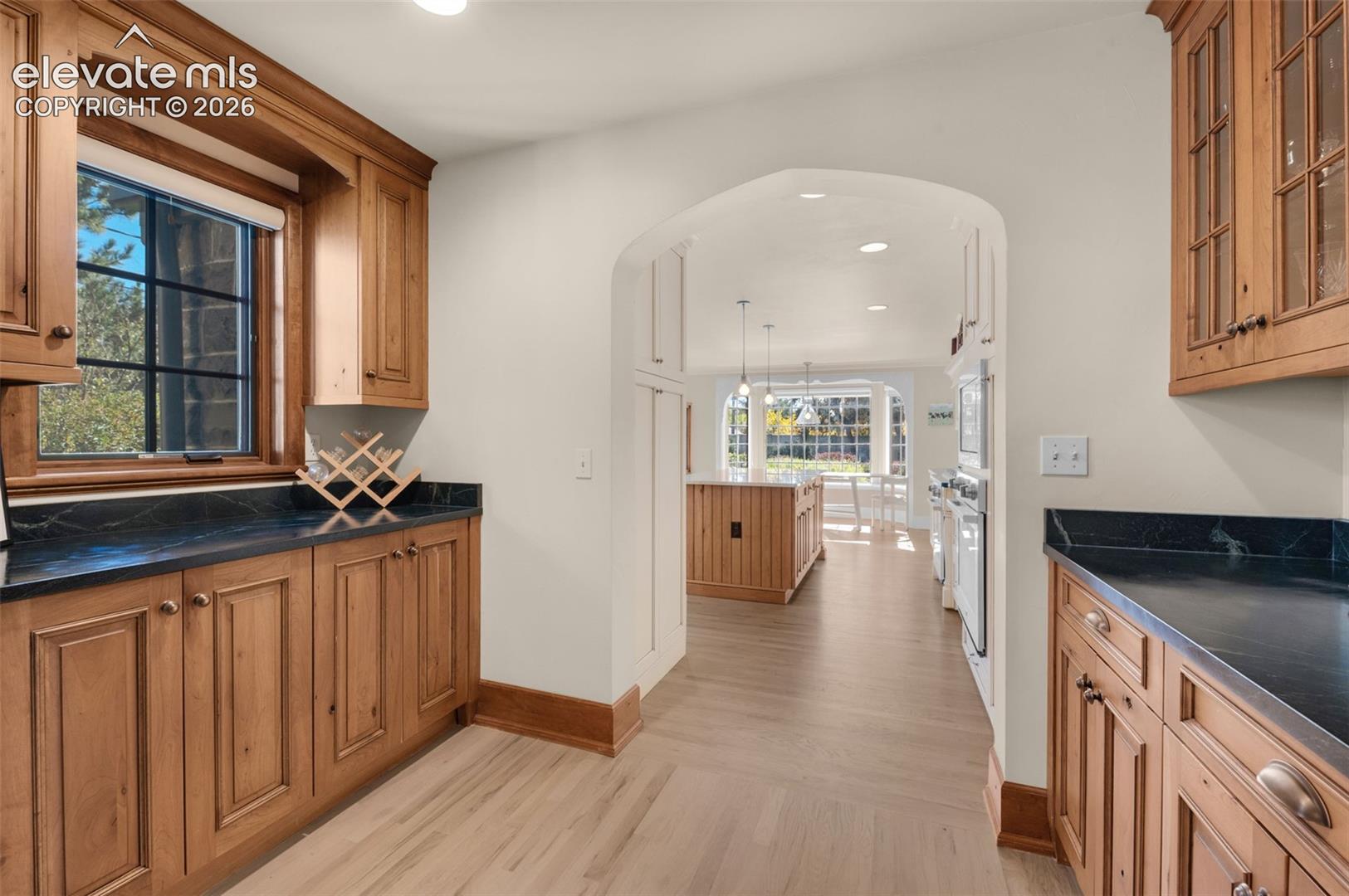 Custom wood cabinetry, dark stone countertops, arched architectural detailing, and light-toned wood-finish flooring