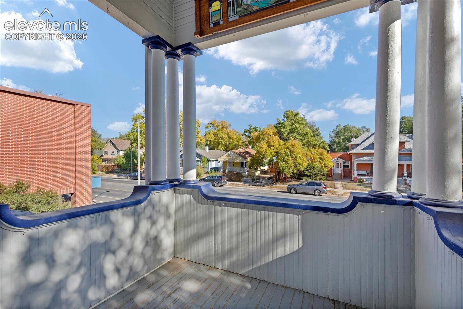 Covered porch featuring vertical tongue-and-groove siding, fluted columns, ornate decorative trim, and stained glass detailing