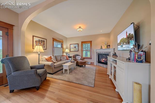 Living room with a tiled fireplace, light wood finished floors, arched walkways, and a baseboard radiator