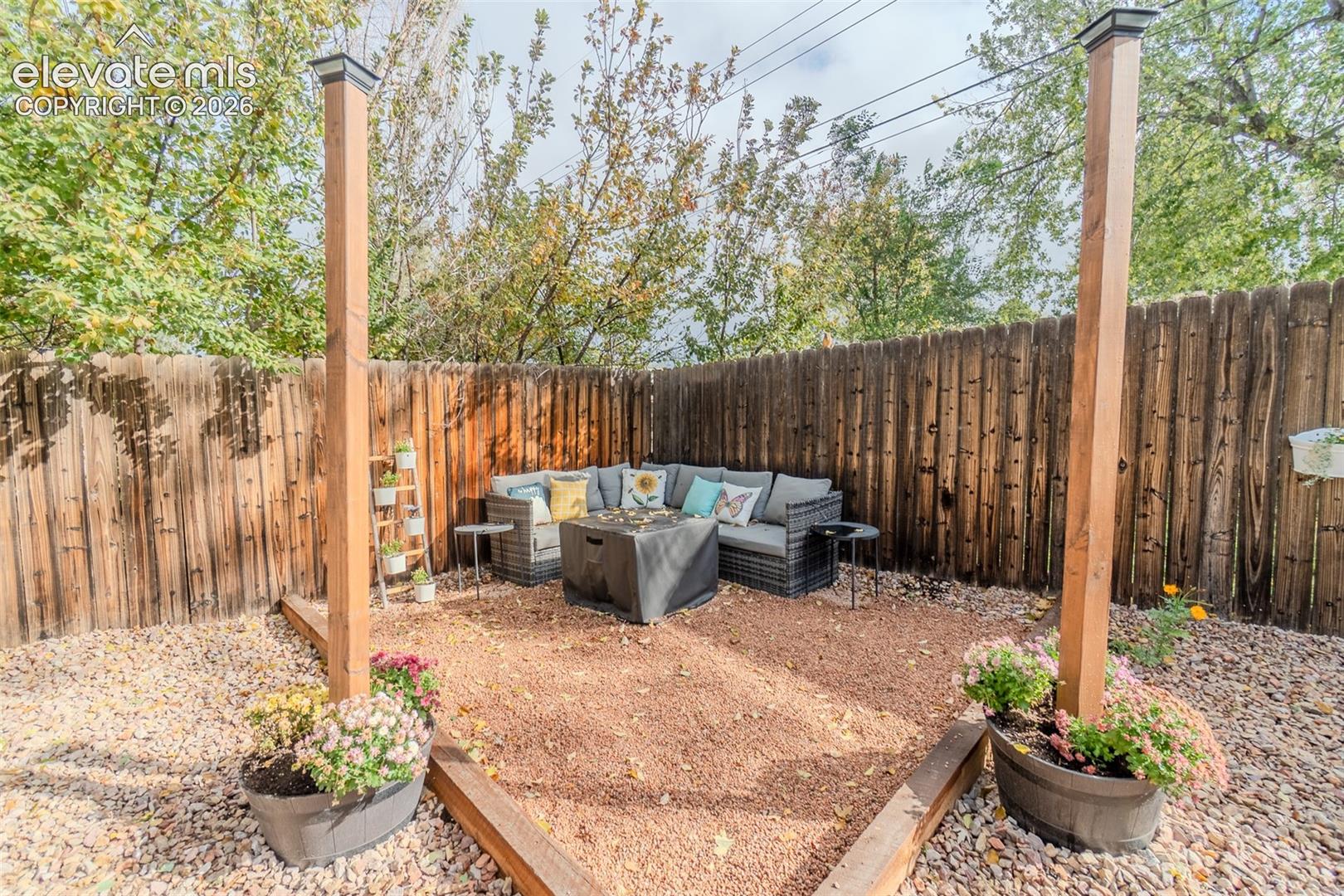 Outdoor space featuring a gravel-surfaced patio area with raised wood-frame borders, tall wooden support posts, and a full-height privacy fence