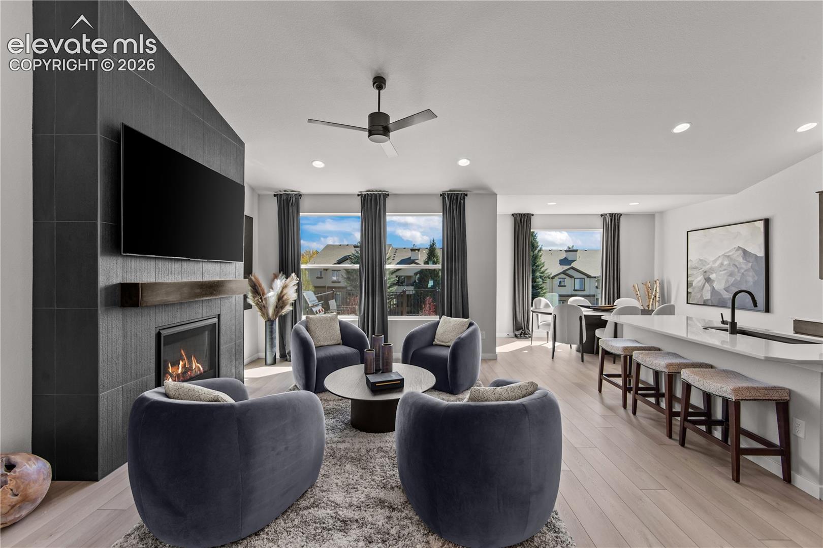 Vaulted ceiling living area featuring a floor-to-ceiling charcoal tile fireplace surround with an integrated mantel, wood-finish flooring, recessed lighting, and a kitchen island with a stone-surface countertop and undermount sink