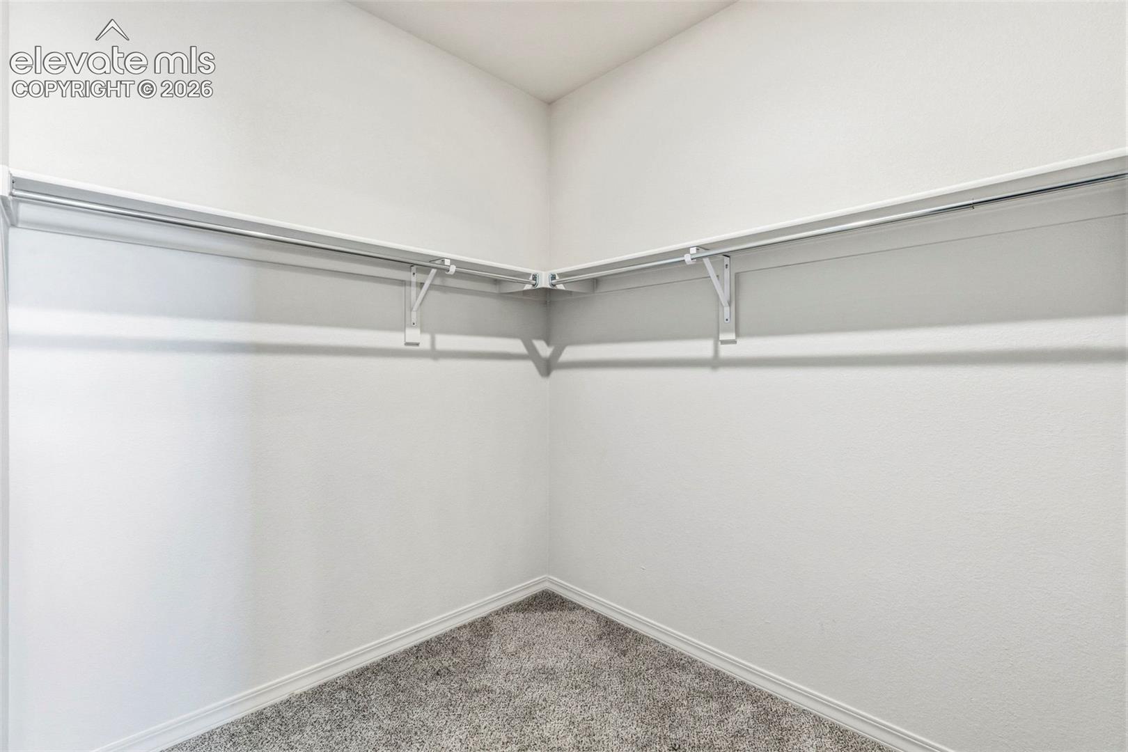 Corner closet featuring white shelving and chrome hanging rods