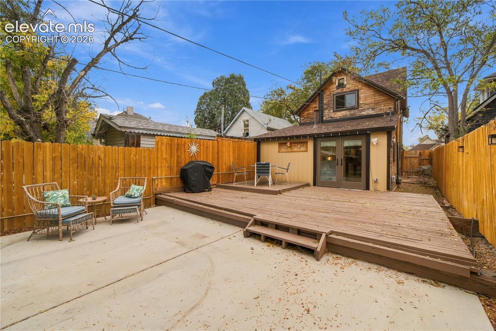Rear exterior featuring a multi-level wood deck, concrete patio, wood privacy fencing, and double glass-pane doors