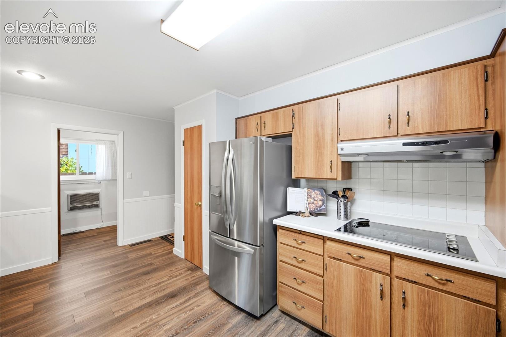Kitchen featuring natural wood-finish cabinetry, solid-surface countertops, square-tile backsplash, built-in stainless steel appliances, and wood-finish flooring