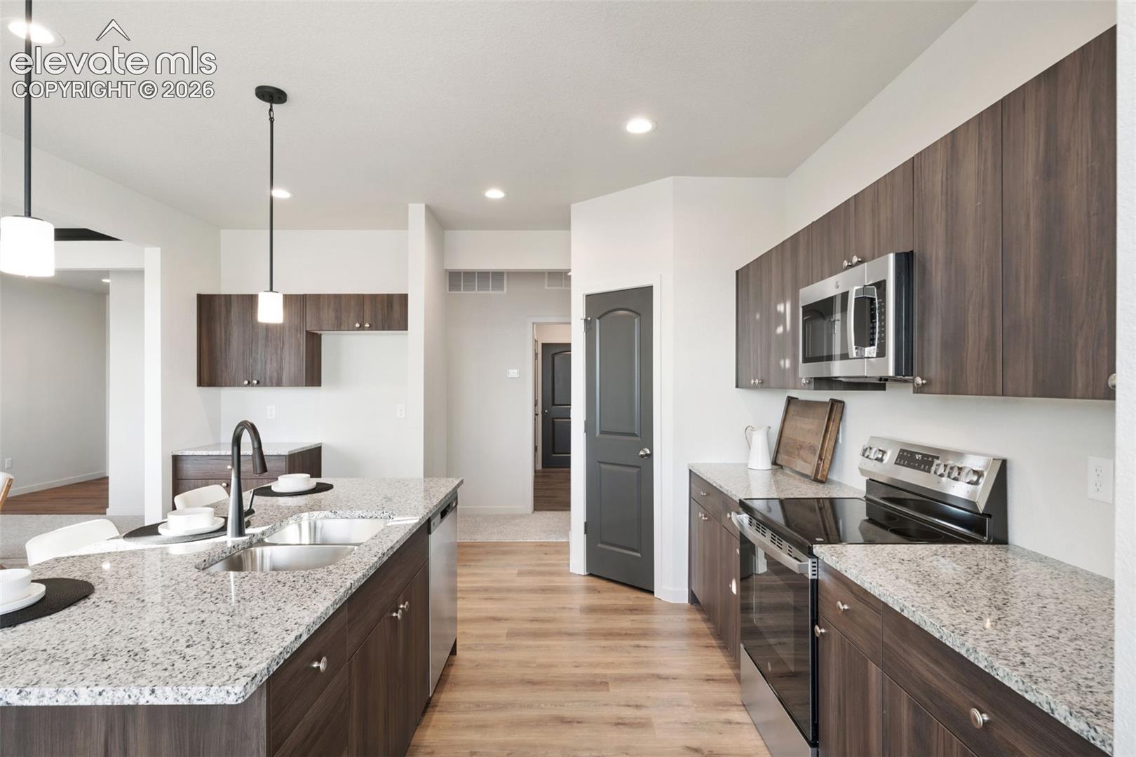 Kitchen featuring wood-finish cabinetry, stainless steel appliances, speckled stone countertops, and wood-finish flooring