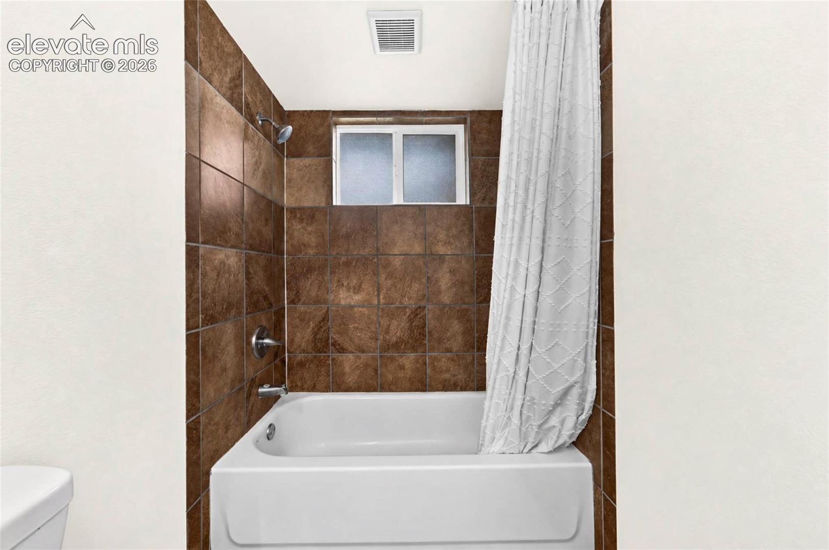 Tub and shower combination featuring dark brown tile surround, a sliding window, and chrome finish fixtures