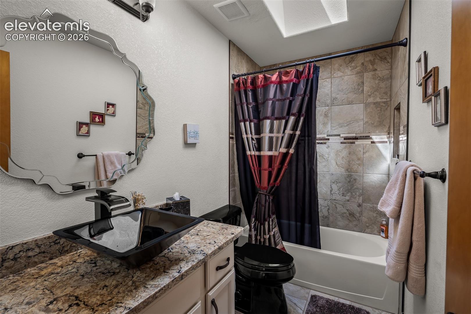 Bathroom featuring a vessel sink with a black faucet, quartz countertop, tiled full bath serving guest bedrooms,